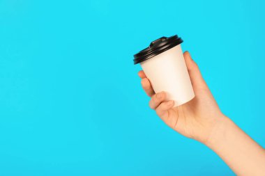 Açık mavi arka planda kağıt bardak tutan kadın, yakın plan. Tasarım için model