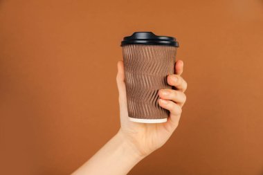 Kahverengi arka planda kağıt bardak tutan kadın, yakın plan. Tasarım için model