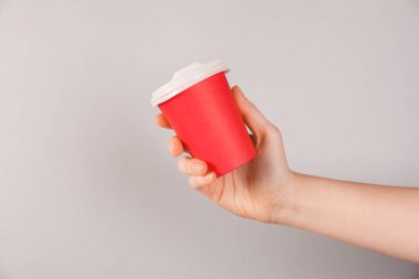 Gri arka planda kağıt bardak tutan kadın, yakın plan. Tasarım için model