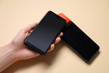 Akıllı telefonu olan bir kadın bej arka planda ödeme terminalini kullanıyor.