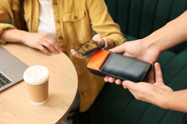 Kafedeki terminalden akıllı telefonla ödeme yapan kadın, yakın plan.