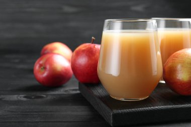 Elma suyunu bardaklarda tazeliyorum ve meyveleri siyah ahşap masada, yakın plan.