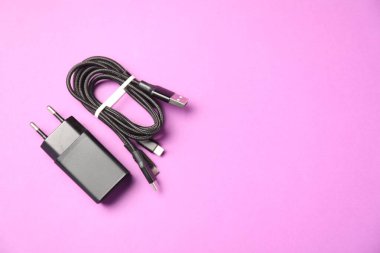 USB güç adaptörü ve mor arka planda üçlü şarj kablosu, düz konum. Metin için boşluk