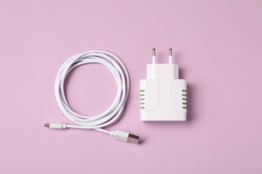 USB güç adaptörü ve pembe arka planda şarj kablosu, düz yatıyordu