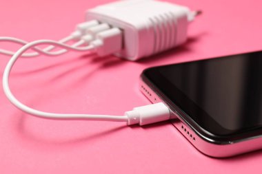 USB şarj kablosu pembe arka plandaki akıllı telefona bağlı, kapat