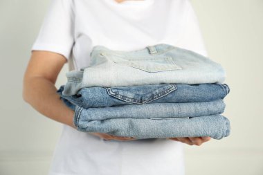 Kapalı alandaki aydınlık duvarın yanında farklı şık kot pantolonları olan kadın, yakın plan.