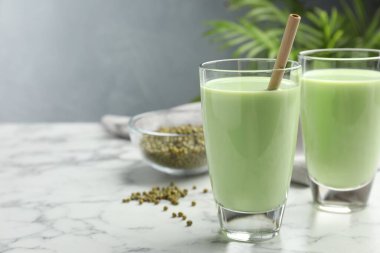 Bardaklarda taze fasulye suyu ve beyaz mermer masada tohumlar, yakın plan. Metin için boşluk