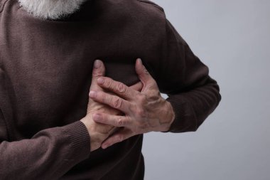 Kalp krizi geçirdi. Gri arka planda göğüs ağrısı çeken son sınıf öğrencisi, yakın plan.
