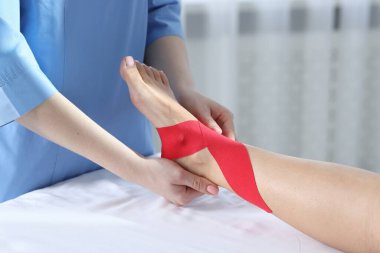 Hastanedeki hastanın ayağına Kinesio bantları takan doktor.