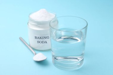 Açık mavi arkaplanda bir bardak su ve kabartma tozu, seçici odak