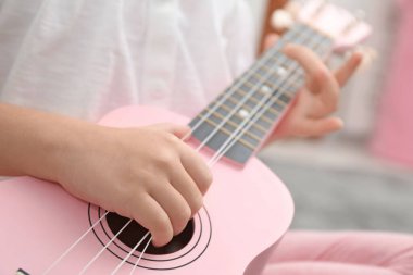 Küçük kız evde ukulele oynuyor, yakın plan.