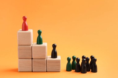 İnsan figürleri, turuncu arka planda üst üste istiflenmiş tahta küplerin üzerine kırmızı olan. Rekabet konsepti