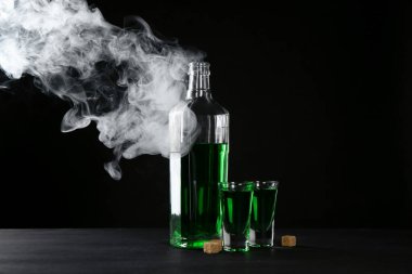 Absinthe shot bardakları, şişe ve esmer şeker siyah arka planda dumanlı
