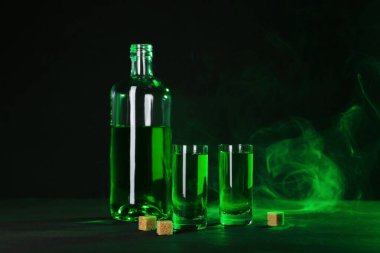 Absinthe shot bardakları, şişe ve esmer şeker siyah arka planda dumanlı