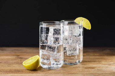Soda suyunu bardaklarda buzla tazelemek ve ahşap masada limonu siyah arka planda kesmek, yakın plan.