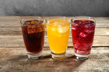 Farklı aromalı soda ve tahta masada buzlu bardaklar.
