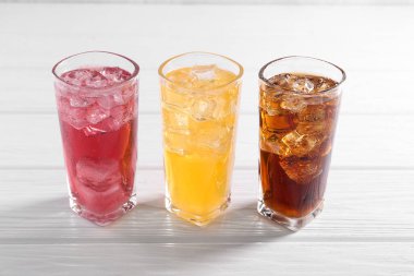 Farklı aromalı soda, beyaz ahşap masada buz küpleri.