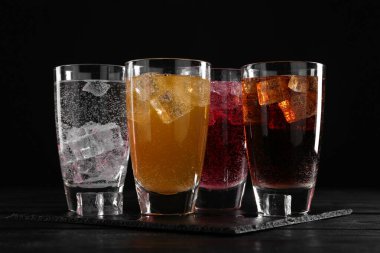 Farklı aromalı soda ve siyah ahşap masada buz küpleri.