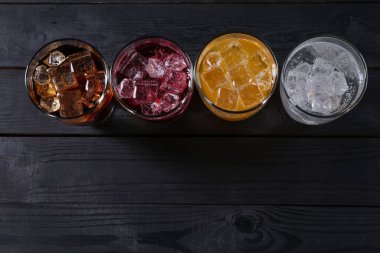Farklı aromalı soda ve siyah ahşap masada buzlu bardaklar. Metin için boşluk