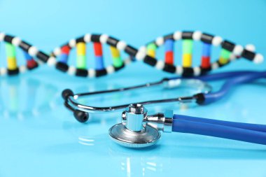 Açık mavi zemin üzerinde stetoskop ve DNA yapısı modeli, yakın plan