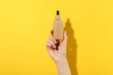 Sarı arka planda serum şişesi olan kadın, yakın plan. Vücut bakımı ürünü