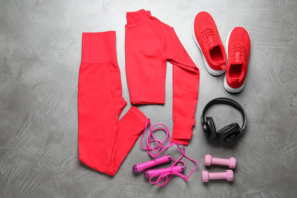 Red sportswear, sneakers, dumbbells and skipping rope on gray textured background, flat lay