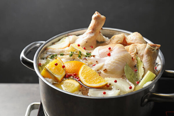Whole fresh turkey, cut citrus fruits and spices boiling in pot on table against black background, closeup