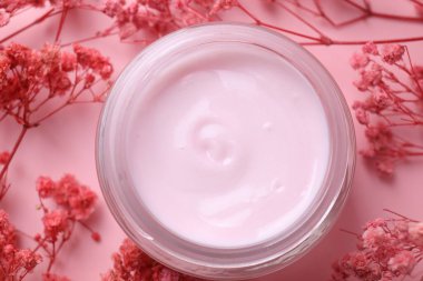 Pembe arka planda çingene çiçekleri arasında bir kavanoz nemlendirici krem.