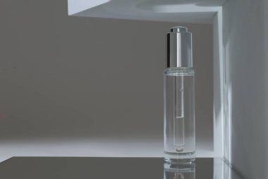 Gri arka planda ayna yüzeyinde bir şişe serum. Metin için boşluk