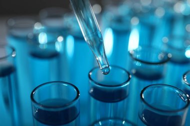 Bulanık arkaplanda test tüplerine sıvı damlatılıyor.