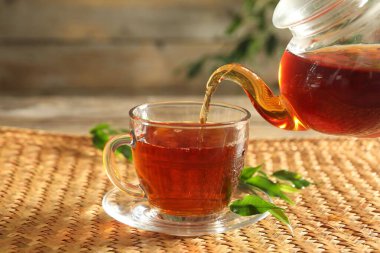 Çaydanlıktan cam fincana taze demlenmiş çay dökülüyor ahşap masada, yakın plan.