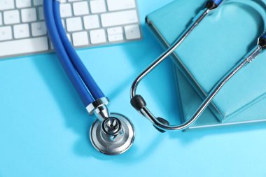Stetoskop, klavye ve açık mavi arkaplan üzerine kitaplar, düz konum