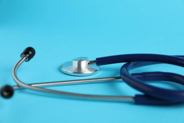 Açık mavi arka planda steteskop, yakın plan. Tıbbi araç