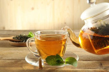 Çaydanlıktan cam fincana taze demlenmiş çay dökülüyor ahşap masada, yakın plan.