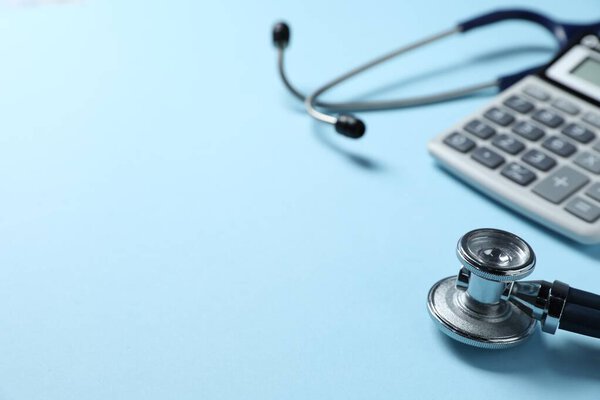 Stethoscope and calculator on light blue background, closeup. Space for text