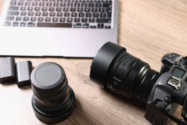 Profesyonel fotoğraf makinesi, lens ve laptop ahşap masanın üstünde.