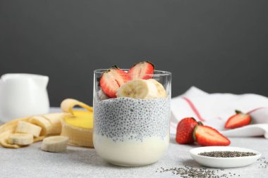 Çilekli lezzetli chia pudingi ve açık gri masada cam içinde muz.