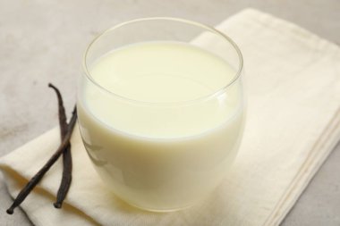 Açık gri masada bir bardak süt ve vanilya kabuğu, yakın plan.