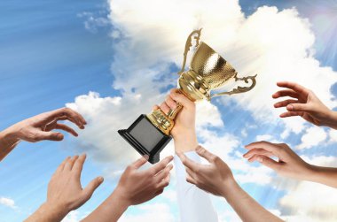 Altın kupa tutan adam ve gökyüzüne uzanan insanlar.