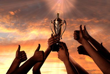 Elinde altın kupa tutan kadın ve günbatımı gökyüzüne başparmak gösteren insanlar, yakın çekim.
