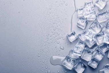 Buz küpleri ve su damlaları açık mavi arkaplanda, düz bir zeminde. Metin için boşluk