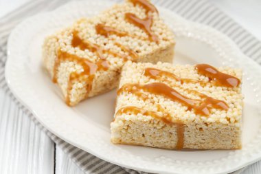 Lezzetli karamelli pirinç çubukları beyaz ahşap masada, yakın plan.