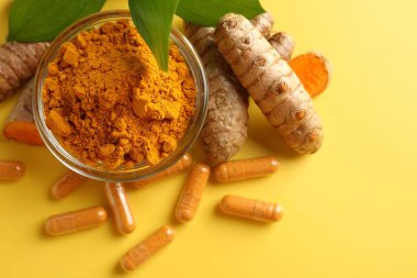 Sarı zemin üzerinde zerdeçal kapsülleri, toz, kökler ve yeşil yapraklar, düz zemin