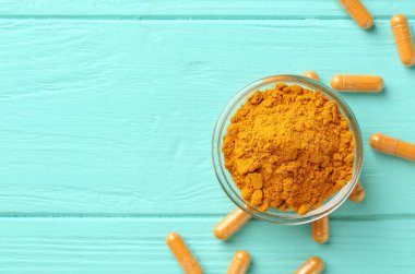 Turkuaz ahşap masa üzerinde zerdeçal kapsülleri ve pudra düz yerde. Metin için boşluk