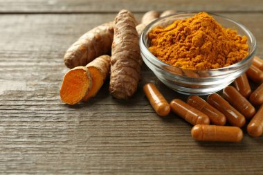 Zerdeçal kapsülleri, toz ve kökler ahşap masanın üzerinde, yakın plan. Metin için boşluk