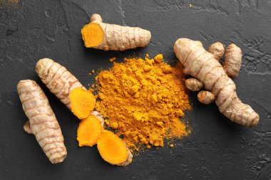 Aromatik zerdeçal tozu ve siyah masanın üzerinde taze kökler.