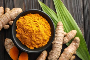 Akvaryumdaki Aromatik zerdeçal tozu, taze kökler ve ahşap masa üzerindeki yapraklar, düz uzanmış.