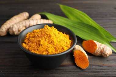 Kasede akromatik zerdeçal tozu, taze kökler ve ahşap masadaki yapraklar, yakın plan.