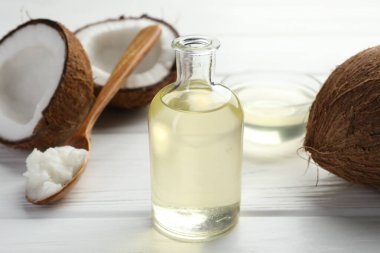 Beyaz ahşap masada organik hindistan cevizi pişirme yağı, kaşık ve taze meyveler, yakın plan.