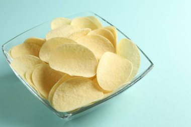 Açık mavi arka planda leziz patates cipsi, yakın plan.